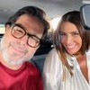 Murilo Benício e Giovanna Antonelli sorridentes, lado a lado, dentro de um carro; ele usa camiseta vermelha e óculos, e ela usa uma blusa branca