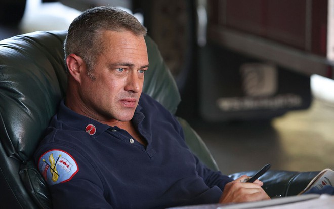 Taylor Kinney está sentado em poltrona com expressão séria em cena de Chicago Fire