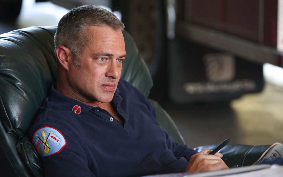 Taylor Kinney está sentado em poltrona com expressão séria em cena de Chicago Fire