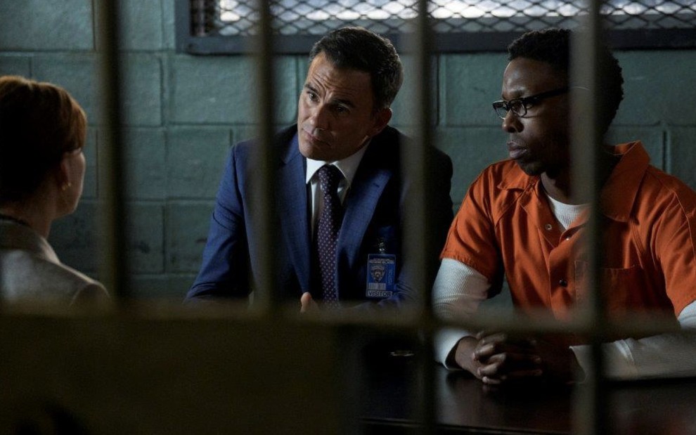 Vestido com terno e gravata, Juan Pablo Raba está ao lado de um jovem negro com macacão de presidiário laranja em cena de Law & Order: SVU