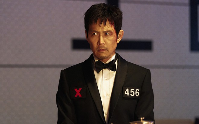Lee Jung-jae tem expressão séria em cena de Round 6; ele veste um terno preto e tem o rosto levemente ensanguentado