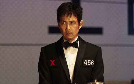 Lee Jung-jae tem expressão séria em cena de Round 6; ele veste um terno preto e tem o rosto levemente ensanguentado