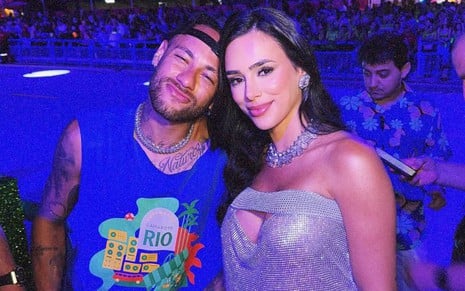 Neymar e Bruna Biancardi lado a lado na Sapucaí; ele usa abadá azul, e faz bico para a foto, e ela usa vestido prata e sorri