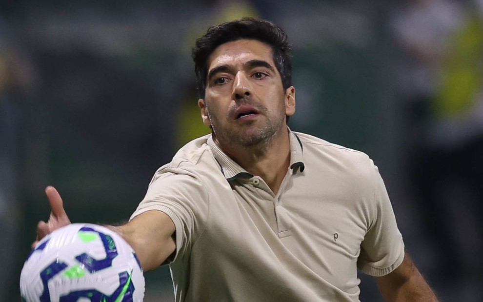 O técnico Abel Ferreira faz movimento para segurar a bola em jogo do Palmeiras; ele usa uma camisa polo bege