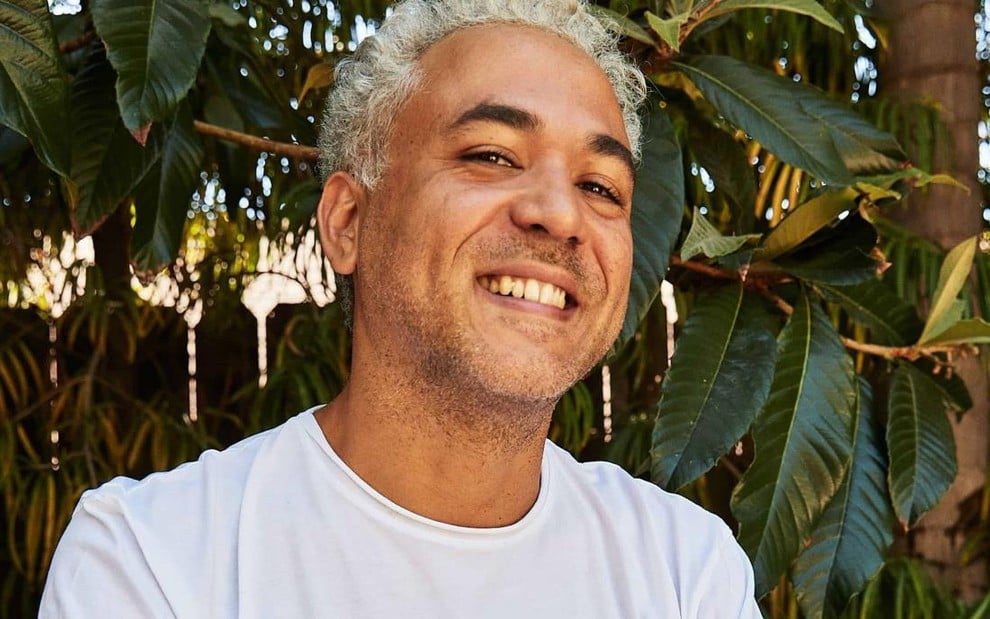 Oz Rodriguez está sorrindo, em uma paisagem com folhas ao fundo