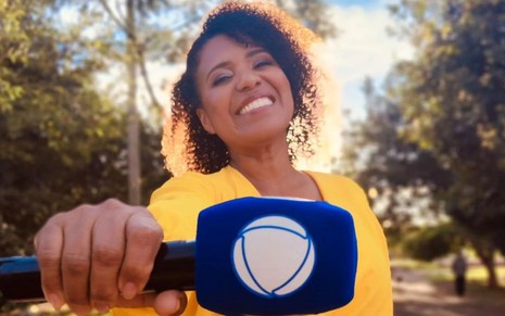 Foto de Érika Leal sorridente com um microfone com a logo da Record em mãos