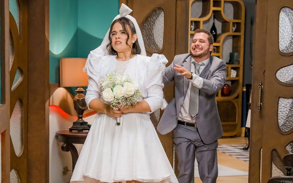 Elisa (Pamella Machado) e César (Andrey Lopes) vestidos de noivos em cena da novela A Caverna Encantada