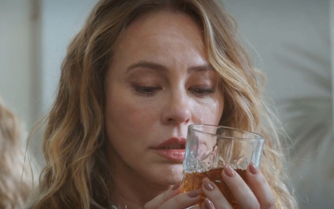 Paolla Oliveira segura um copo com bebida na frente do rosto em cena como Heleninha na novela Vale Tudo