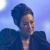 Michelle Yeoh está sentada à mesa, com os braços abertos e um visual futurista