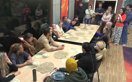 Os participantes do Power Couple Brasil estão reunidos ao redor de mesa