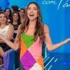 Patricia Abravanel está com braços abertos no meio da plateia do Programa Silvio Santos; ela usa vestido com recortes coloridos