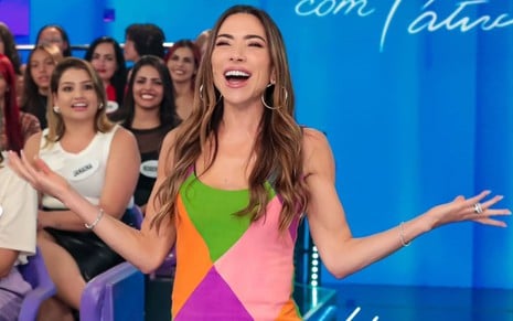 Patricia Abravanel está com braços abertos no meio da plateia do Programa Silvio Santos; ela usa vestido com recortes coloridos