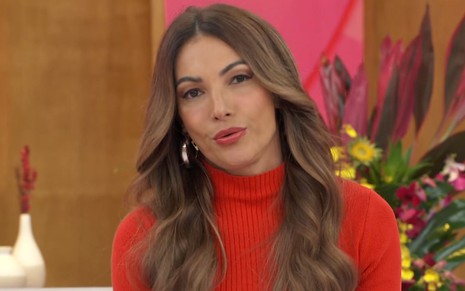 Patrícia Poeta sentada no cenário do Encontro, usando vestido vermelho com gola alta