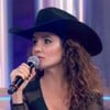 Paula Fernandes, de chapéu preto, segura um microfone com a mão direita no palco do Caldeirão com Mion