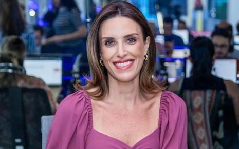 Paula Monteiro sorri, com uma redação jornalística no fundo da imagem