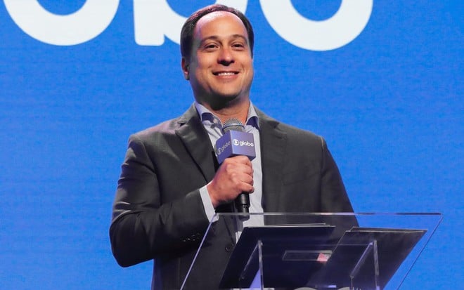 Paulo Marinho sorri e segura microfone com o logo da Globo em evento