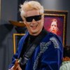 Pedro Lemos está com os braços levantados e usa uma guitarra pendurada no corpo; várias crianças estão ao redor dele