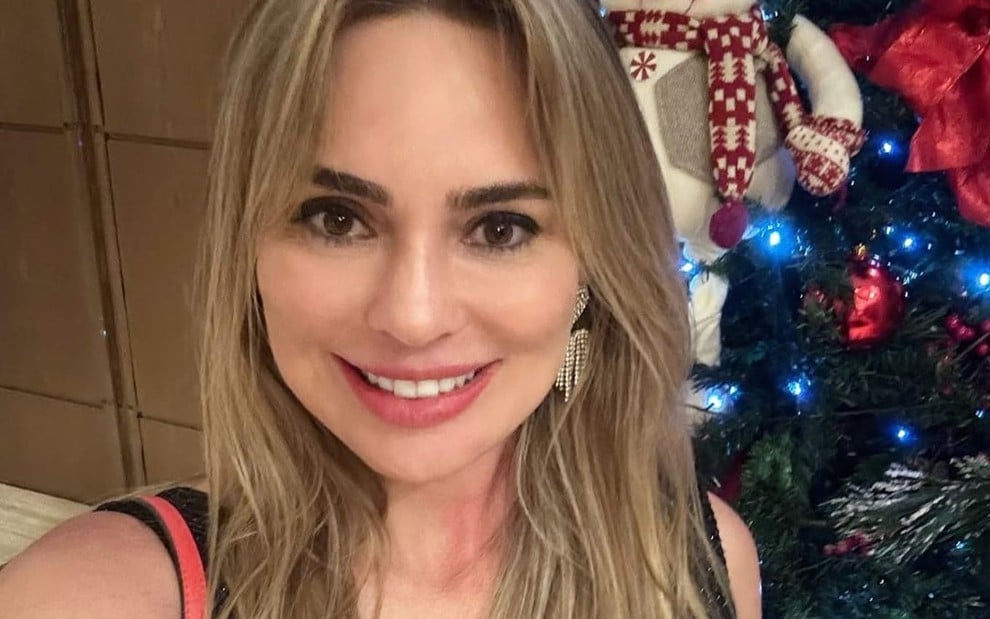 Rachel Sheherazade posa ao lado de uma árvore de Natal; ela sorri para a câmera