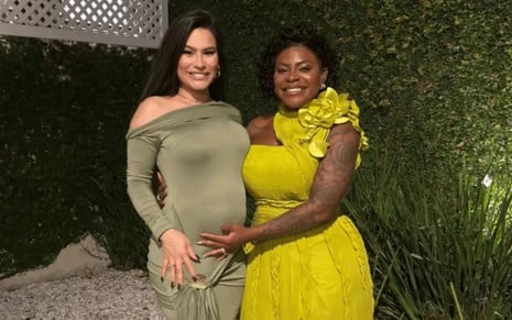 Raissa Barbosa e Jojo Todynho juntas; Raissa usa vestido verde-musgo e Jojo usa vestido amarelo e coloca a mão na barriga da amiga