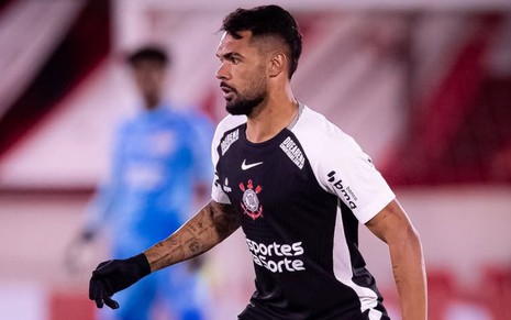 Jogador do Corinthians em campo, usando uniforme preto e branco com luvas pretas, em ação durante partida de futebol.