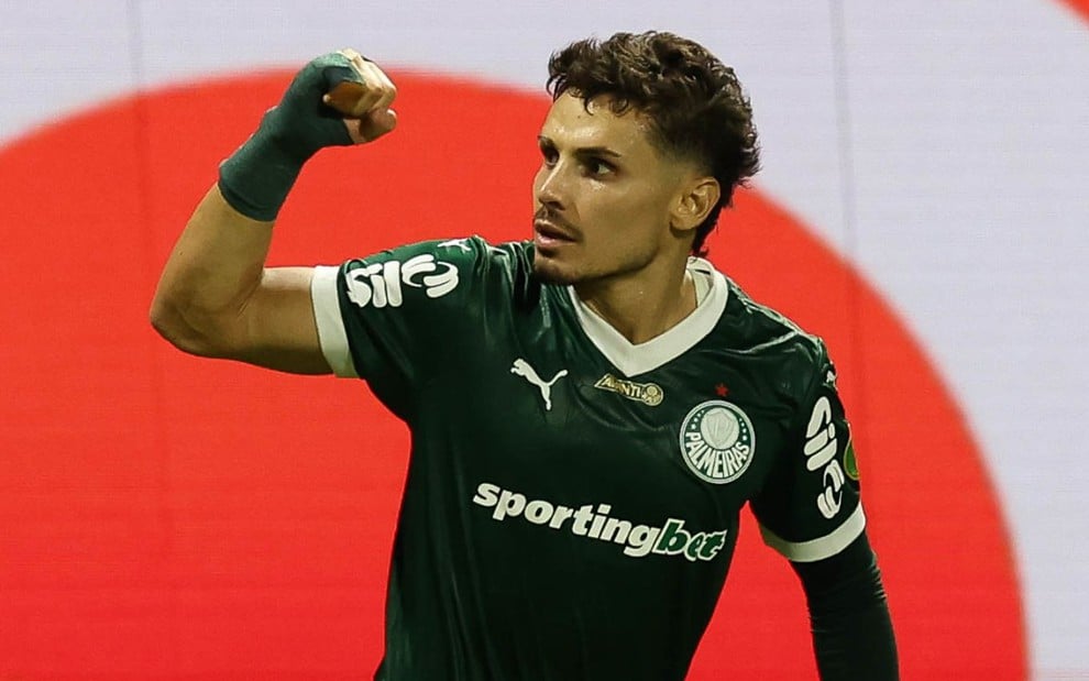 Raphael Veiga usa o uniforme verde do Palmeiras e está com braço levantado em sinal de força