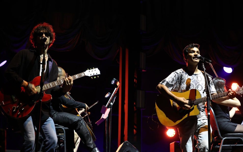 Ravel Andrade e Tony Gambel em painel da CCXP 24 sobre a série Raul Seixas: Eu Sou, cantando e tocando guitarra