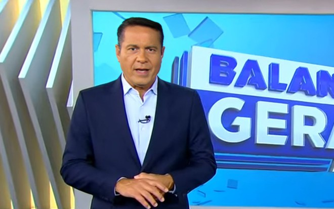 Um homem de terno e gravata em frente a um telão em que se lê: BALANÇO GERAL MANHÃ