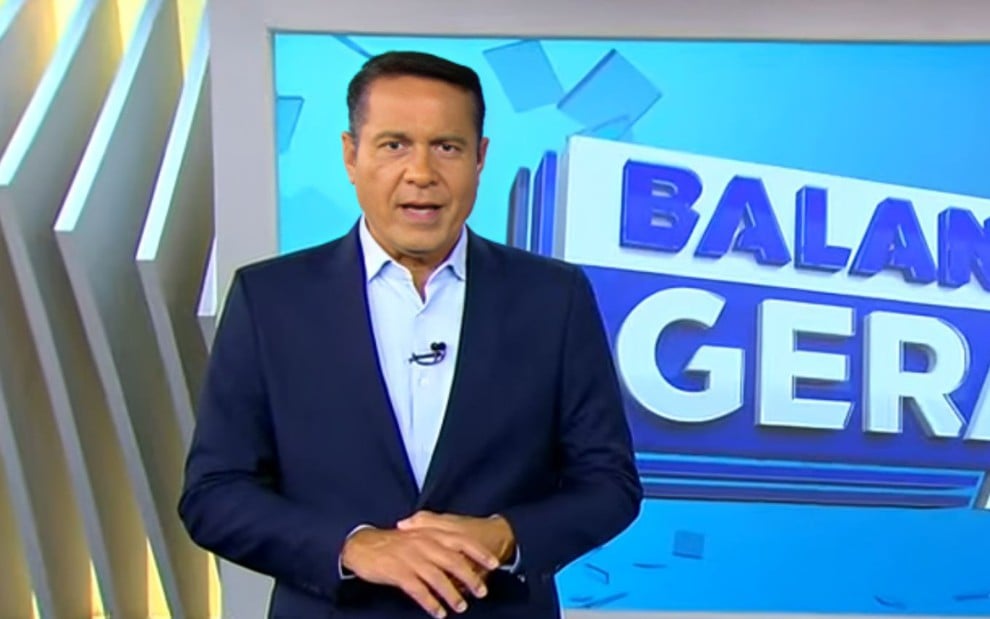Um homem de terno e gravata em frente a um telão em que se lê: BALANÇO GERAL MANHÃ