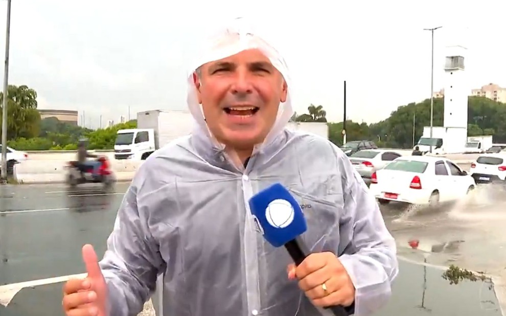 Reinaldo Gottino com capa de chuva e um microfone da Record no meio de uma tempestade no Cidade Alerta