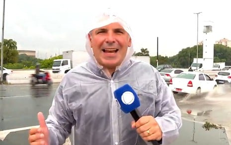 Reinaldo Gottino com capa de chuva e um microfone da Record no meio de uma tempestade no Cidade Alerta