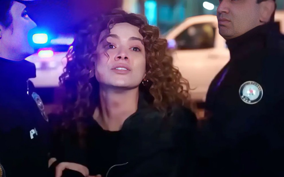 A atriz Serya Kaya como Sirin é segurada por dois policiais em cena de Força de Mulher
