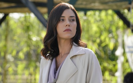 Mulher com casaco creme tem expressão nervosa em cena da novela Iludida