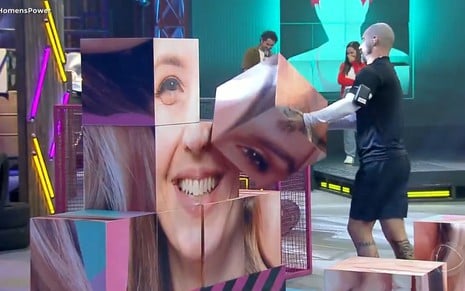 Radamés segura cubo com o rosto de uma mulher no cenário de provas do Power Couple