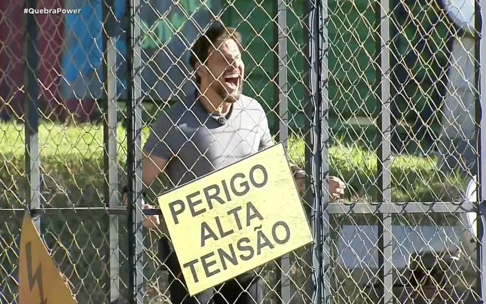Rafael Pessina está dentro de uma gaiola com uma placa de "Perigo: Alta Tensão" na grade
