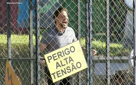 Rafael Pessina está dentro de uma gaiola com uma placa de "Perigo: Alta Tensão" na grade