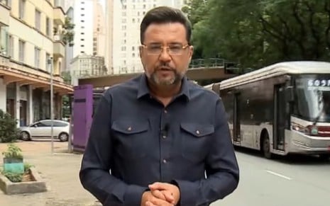 Geraldo Luís está numa calçada, com um ônibus passando ao fundo; ele tem expressão séria