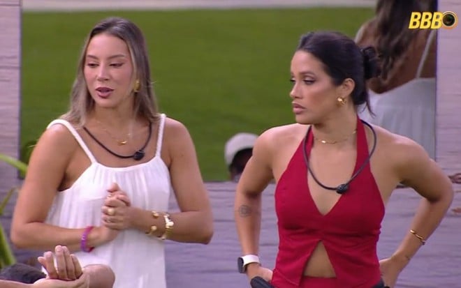 Renata e Eva lado a lado, no lado externo da casa do BBB 25; à esquerda, Renata usa vestido branco, à direita, Eva está de blusa decotada vermelha e calça preta