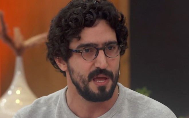 Renato Góes sentado no sofá do Encontro, usando óculos e camiseta cinza