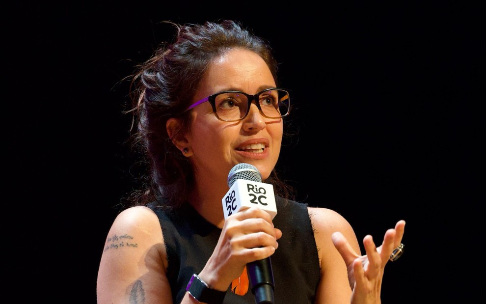 Manuela Dias fala em microfone em um fundo preto no Rio2C