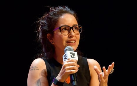 Manuela Dias fala em microfone em um fundo preto no Rio2C