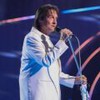 Roberto Carlos cantando em um palco à frente de um microfone; ele está de perfil
