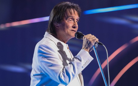 Roberto Carlos cantando em um palco à frente de um microfone; ele está de perfil