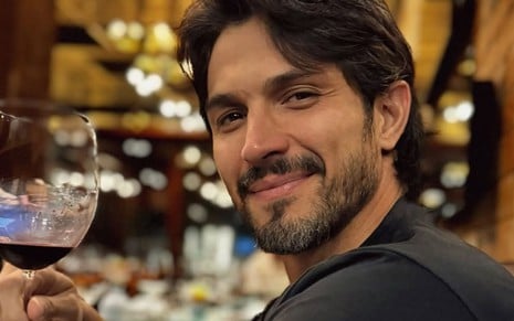 Romulo Estrela posando com sorriso leve, segurando uma taça de vinho