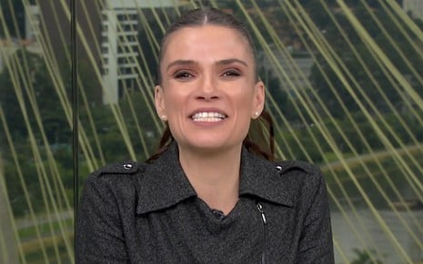 Sabina Simonato sorridente no Bom Dia Brasil, usando uma jaqueta preta com detalhes em prata