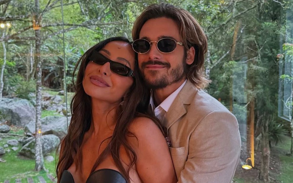 Sabrina Sato e Nicolas Prattes estão abraçados e sorridentes, com óculos de sol