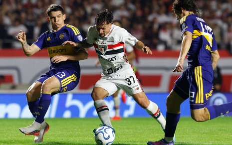 O jogador do São Paulo, vestindo a camisa 37, domina a bola no gramado enquanto é marcado por dois adversários do Boca Juniors