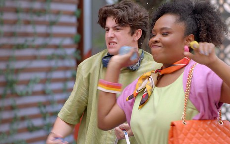Henrique Sganzerla e Ariane Souza arremessam bexigas cheias d'água na direção de alguém em cena de A Caverna Encantada