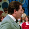 Silvio Santos conversa com uma mãe que segura uma criança no colo no cenário do Domingo no Parque