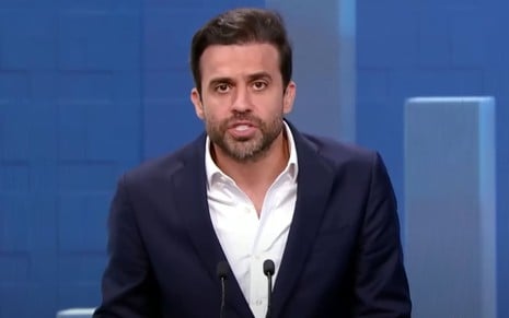 Pablo Marçal usa um blazer preto e uma camisa social branca; ele está sério