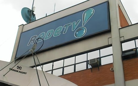 Fachada do edifício da emissora RedeTV!, destacando um painel azul no topo com o logótipo do canal e antenas parabólicas visíveis em primeiro plano.